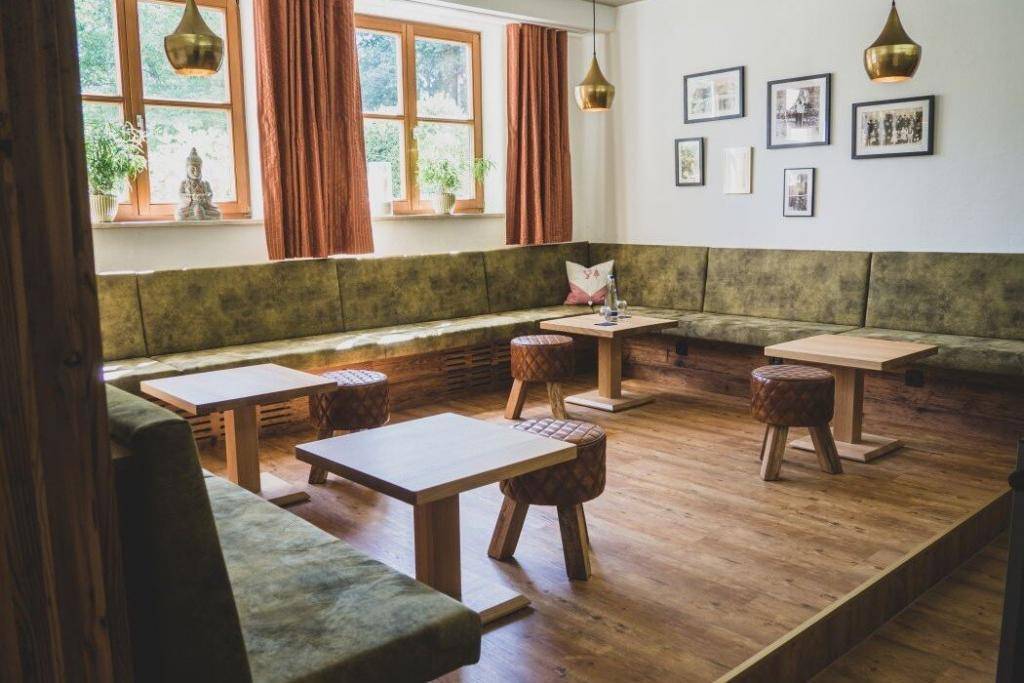 Das Foyer am Konferenzraum Quelle: umlaufende grüne Polsterbank, niedrige Holztische, Lederhocker und Messing-Hängeleuchten