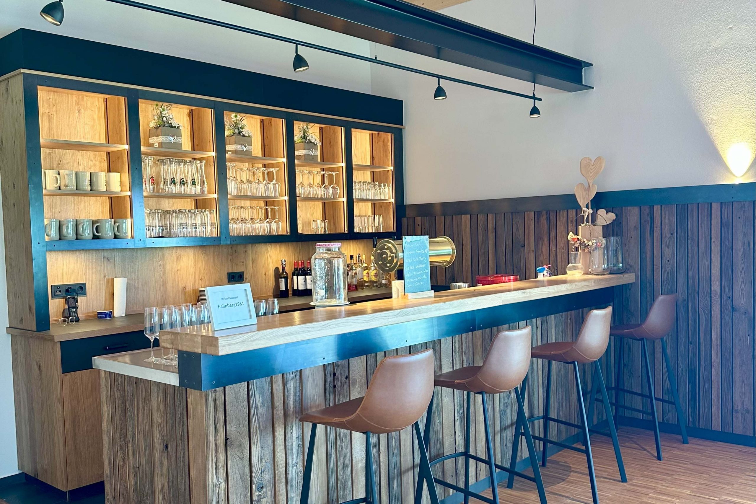 Moderne Bar im Bungalow des Landhotel Hallnberg mit Holzelementen, Tresen und Barhockern.