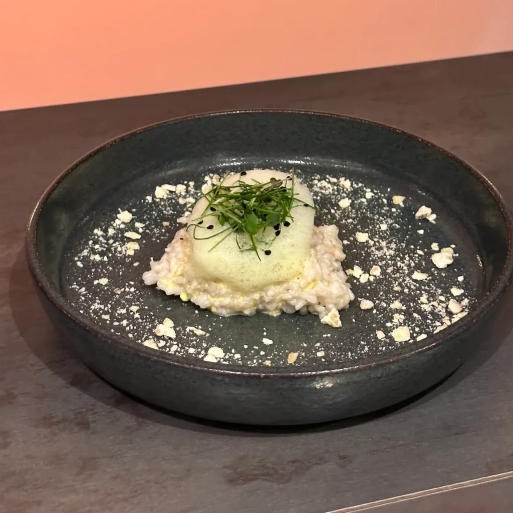 Fein angerichtetes Gericht mit heller Creme und grüner Garnitur auf einem dunklen Teller.