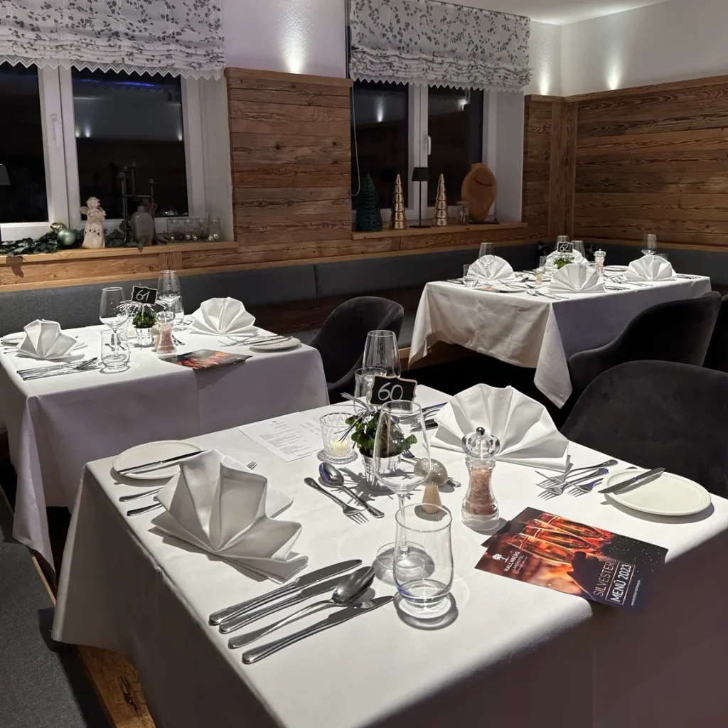 Weiß gedeckte Restauranttische mit gefalteten Servietten vor einer Fensterfront und Holzverkleidung.