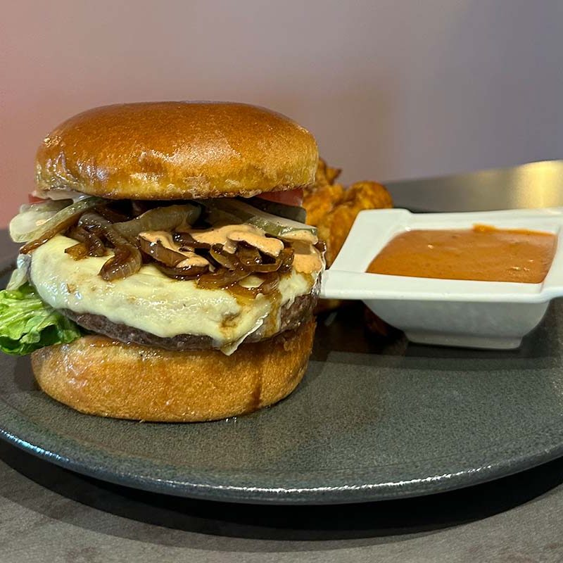 aftiger Cheeseburger mit karamellisierten Zwiebeln, Salat und Brötchen, serviert mit Dip – perfektes Beispiel für die Burger- & BBQ-Variante bei Familienfeiern im Landhotel Hallnberg